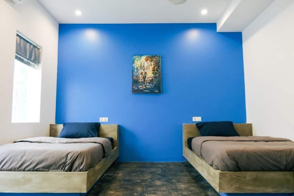 A room with two wooden beds, a blue wall, and a painting.