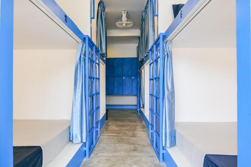 A narrow hallway with bunk beds on either side, a blue door at the end, and a ceiling fan.