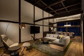 Un salon moderne avec un canapé d’angle, une table basse ronde, un lampadaire et un téléviseur à écran plat fixé au mur.