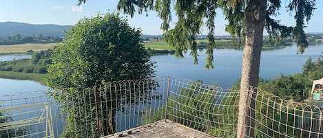 Une terrasse en bois avec deux bancs donnant sur un lac, entourée d’une clôture en fil de fer et d’arbres.