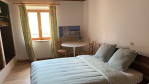 Un dormitorio con una cama, dos sillas, una mesita redonda y una ventana con cortinas.