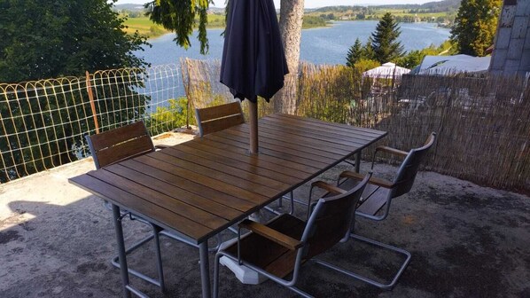 Une terrasse extérieure avec une table et des chaises en bois, une clôture en métal et une vue sur un lac.