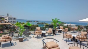 A rooftop terrace with outdoor seating, a clear view of the sea, and surrounding buildings. - L'Amo del Mare Hotel (Ksamil)