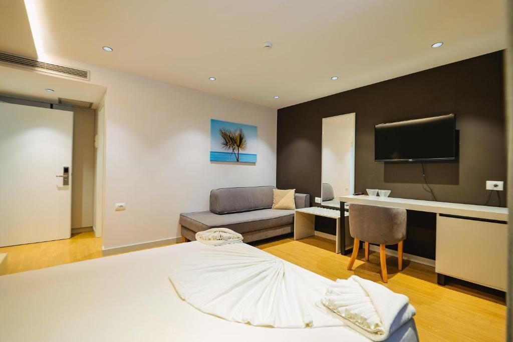 Ett modernt hotellrum med en säng, ett skrivbord, en grå soffa, en tv och en tavla på väggen.