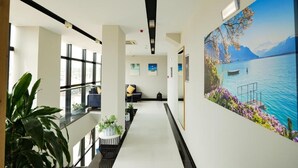 A modern hotel lobby with a large scenic painting, a glass railing, and a seating area with a sofa and chairs. - L'Amo del Mare Hotel (Ksamil)