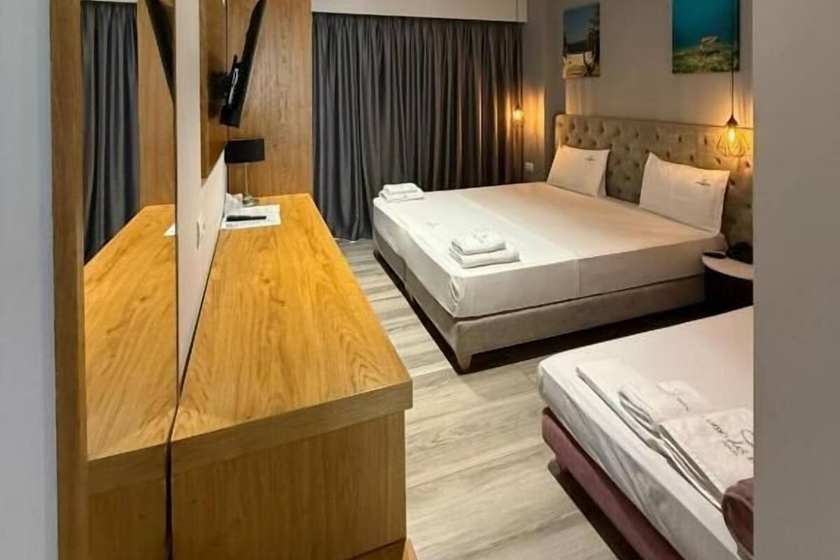 Una habitación de hotel moderna con un escritorio de madera, dos camas, un espejo grande y un cuadro en la pared.