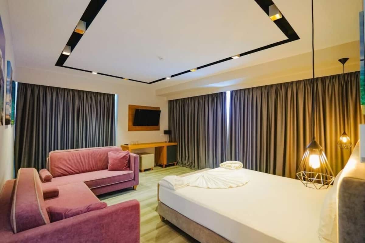 Una habitación de hotel moderna con una cama grande, un sofá rosa, un escritorio y un ventanal con cortinas.