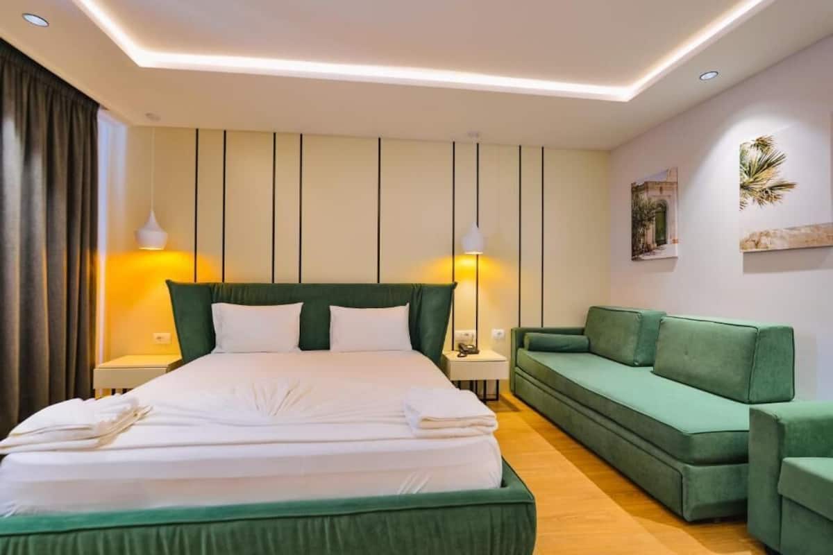 Una habitación de hotel con una cama grande, un sofá verde y dos lámparas de noche.