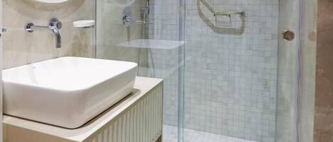 A modern bathroom with a glass-enclosed shower, a round mirror, and a white sink.