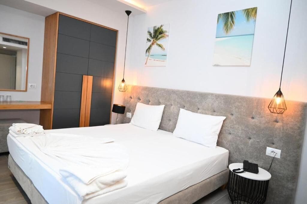 Moderni hotellihuone, jossa on suuri sänky, vaatekaappi, peilillä varustettu meikkipöytä ja taideteoksia seinillä.