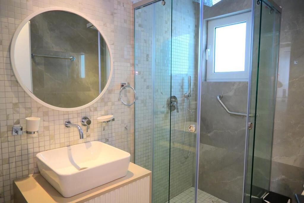 Un bagno con un lavandino bianco, uno specchio rotondo e una cabina doccia in vetro.