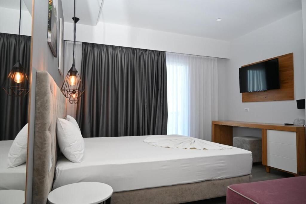 Una habitación de hotel moderna con una cama grande, un escritorio, un televisor y dos lámparas colgantes.