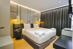 Una habitación de hotel moderna con una cama grande, mesitas de noche, un escritorio y una cortina.