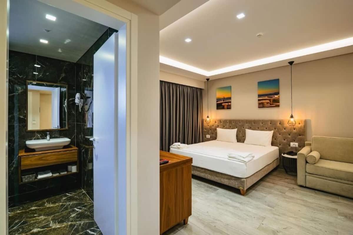 Una habitación de hotel moderna con un baño de mármol, una cama con cabecero y un sofá.