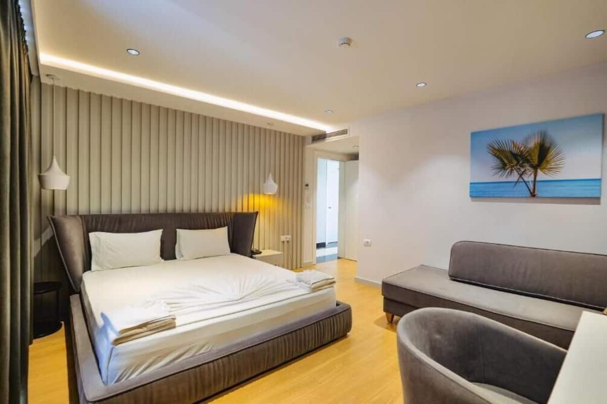 Una habitación de hotel moderna con una cama grande, un sofá y un cuadro de palmeras.