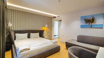 Quarto de hotel moderno com uma cama grande, um sofá e uma pintura de palmeiras.