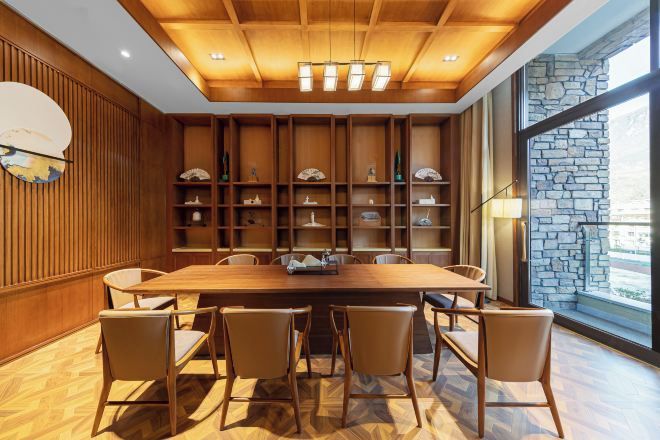A dining area with a wooden table and chairs, a wall-mounted clock, and shelves with decorative items.