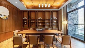 A dining area with a wooden table and chairs, a wall-mounted clock, and shelves with decorative items.