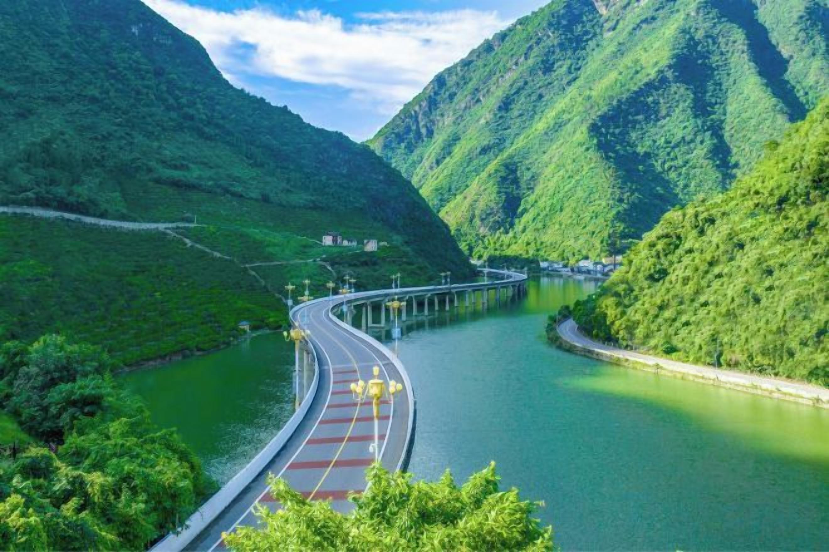 A bridge over a river with a road curving alongside, surrounded by lush green hills.