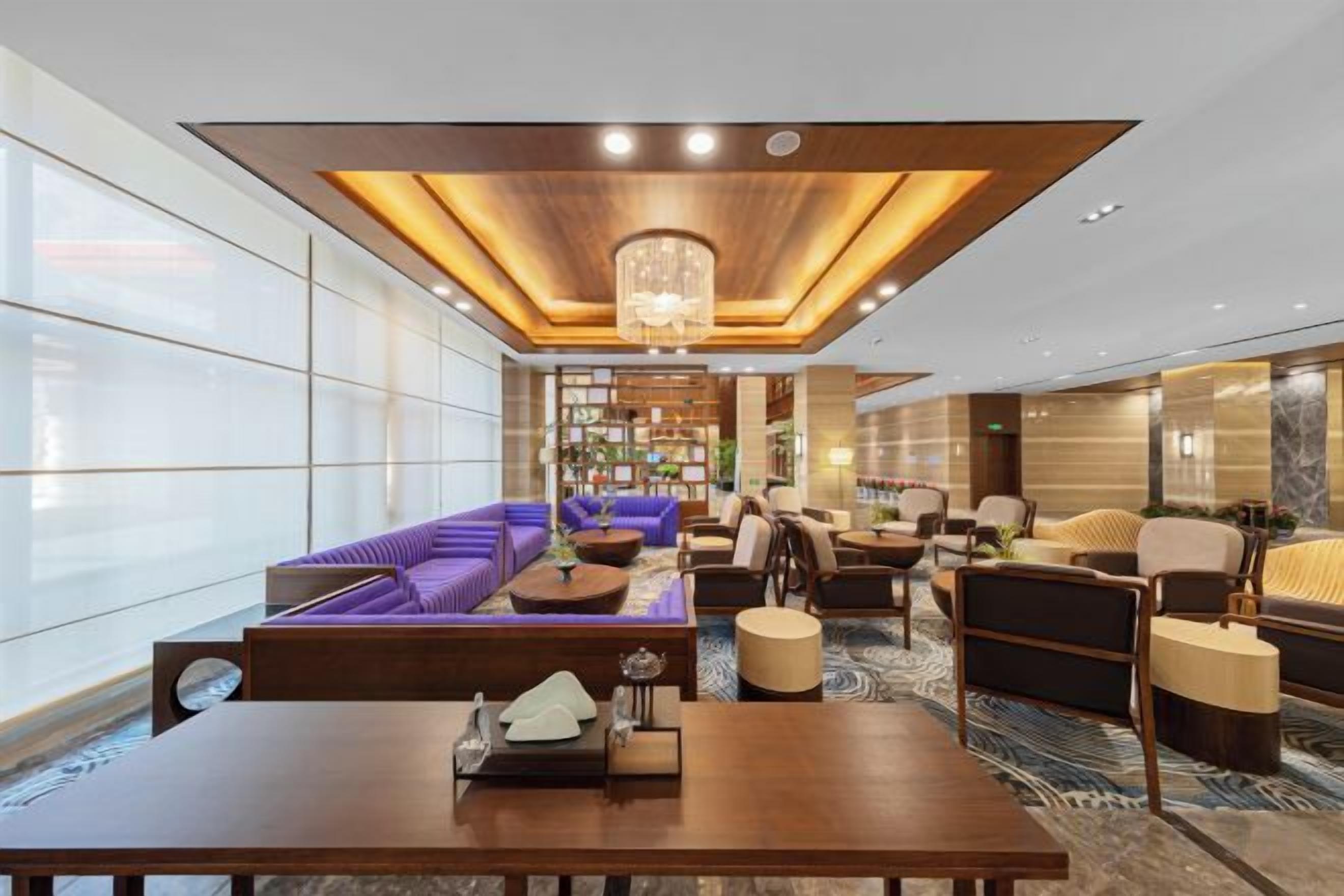 A spacious lobby with a wooden ceiling, a central seating area with sofas, and a large table.