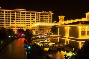 A large hotel with multiple floors and a well-lit facade, a courtyard with a fountain, and a bridge connecting different parts of the property.