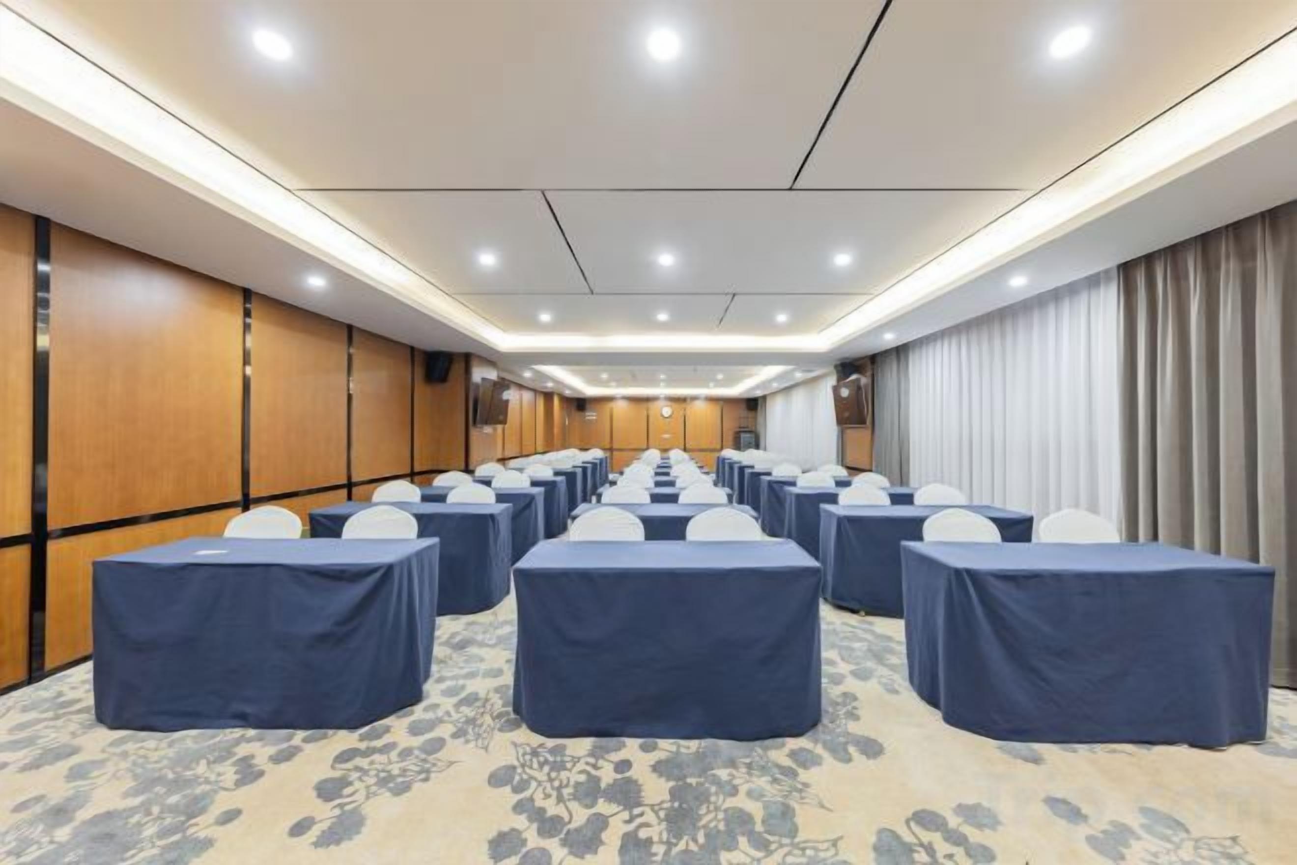 A conference room with rows of tables and chairs, carpeted floor, and wooden paneling on the walls.