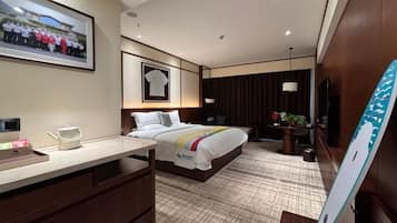 A hotel room with a bed, a desk, a chair, a TV, and a picture on the wall.
