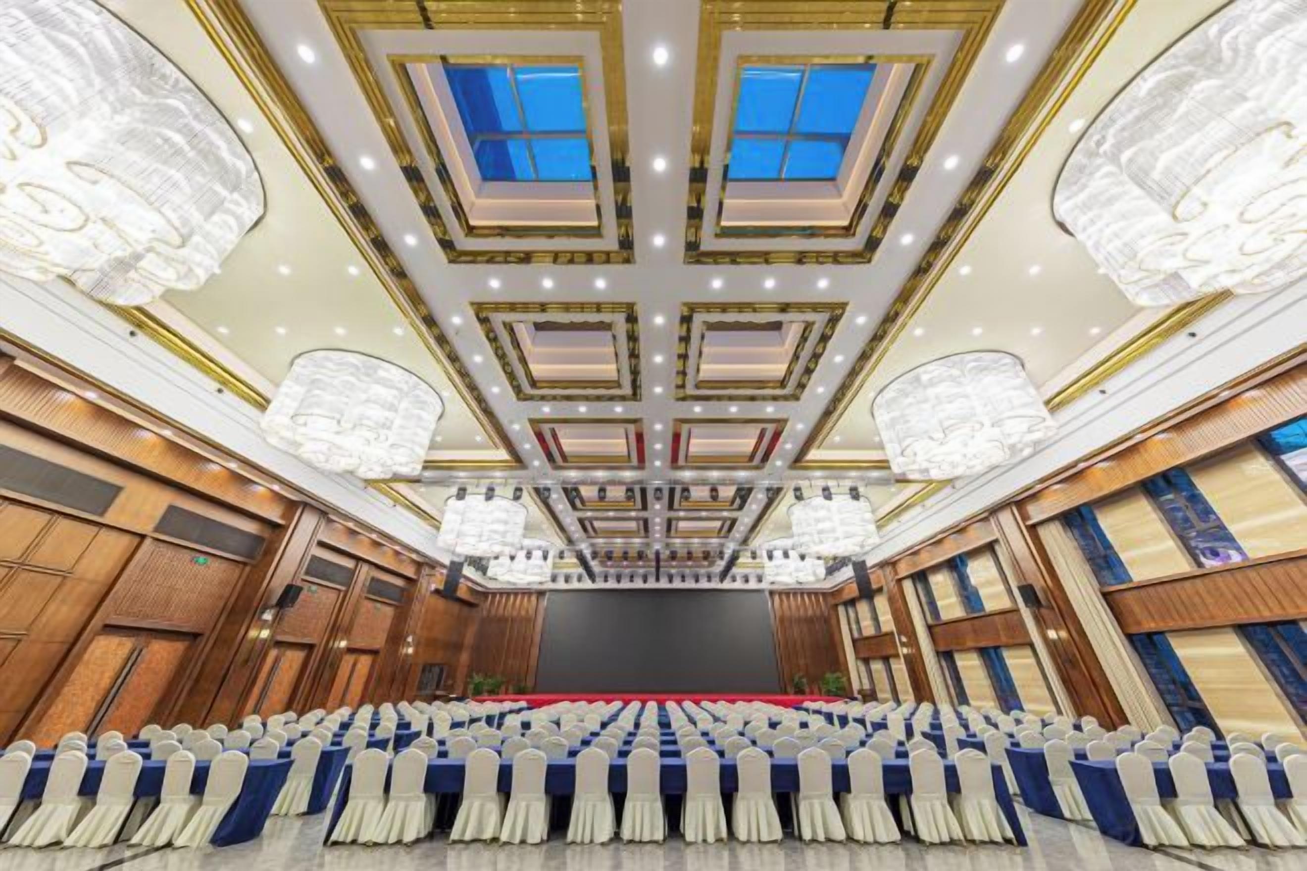 A large conference room with a stage, rows of chairs, and a high ceiling with chandeliers.