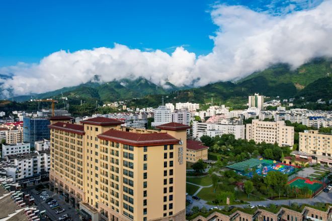 Un paisaje urbano con un edificio destacado, montañas al fondo y cielo despejado.