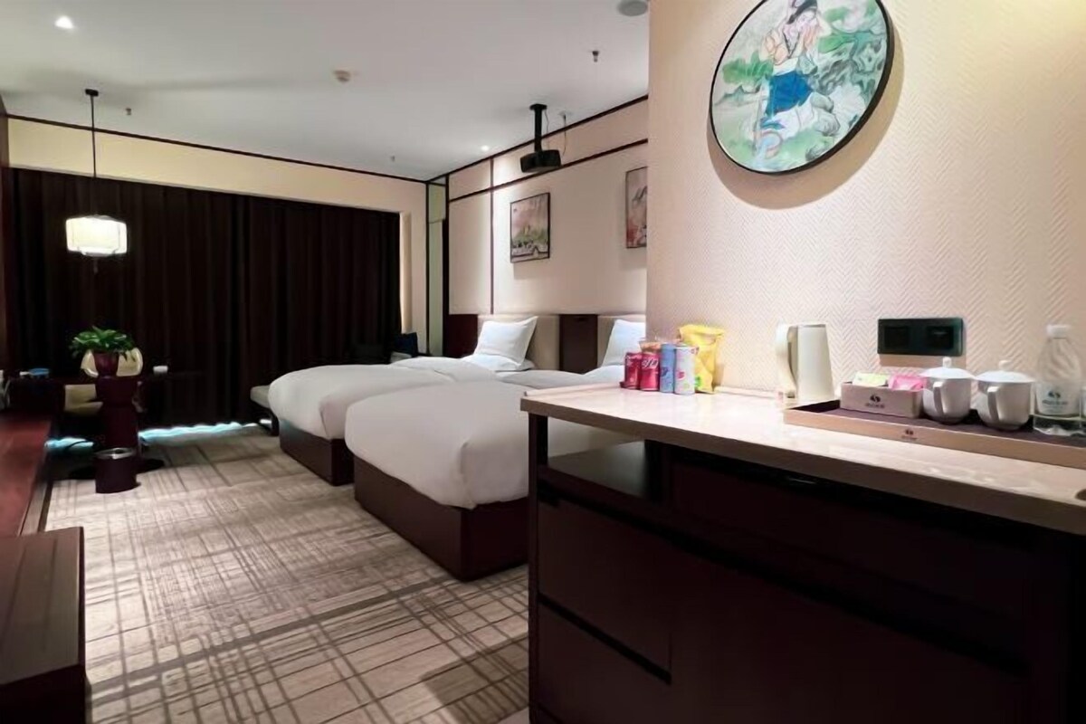 Een hotelkamer met een bed, nachtkastje en een groot schilderij aan de muur.