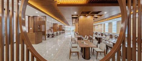 A modern restaurant with a central dining area, wooden paneling, and a curved ceiling design.