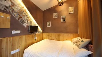 A bedroom with a wooden headboard, a bed with white bedding, a flat-screen TV mounted on the wall, and a small window with curtains.