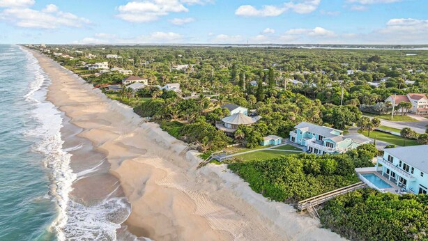 Un quartier résidentiel situé sur la côte, avec des propriétés donnant sur la plage, une piscine et des espaces verts bien entretenus.