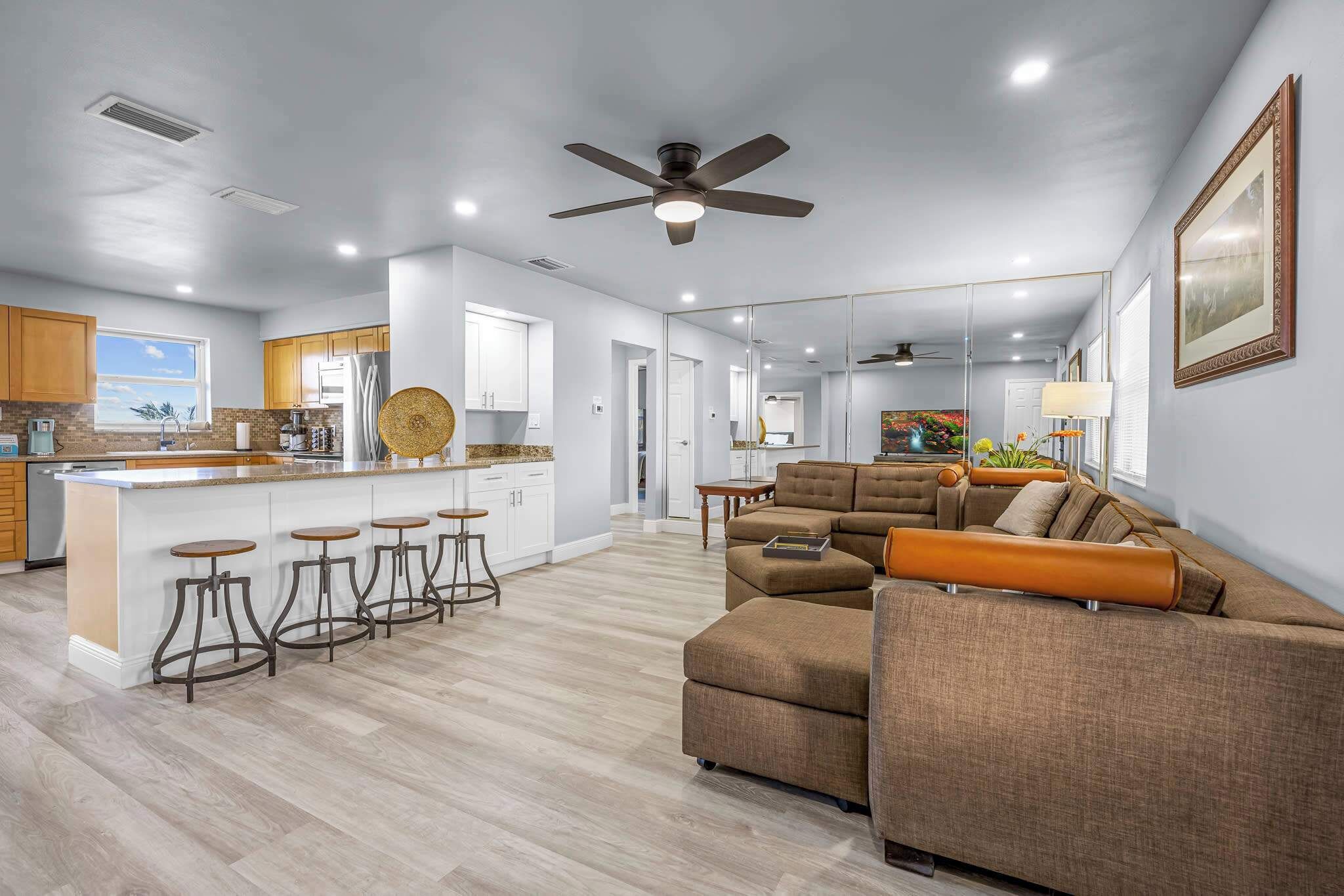 A modern kitchen with a central island, a dining area with a sofa, and a ceiling fan.
