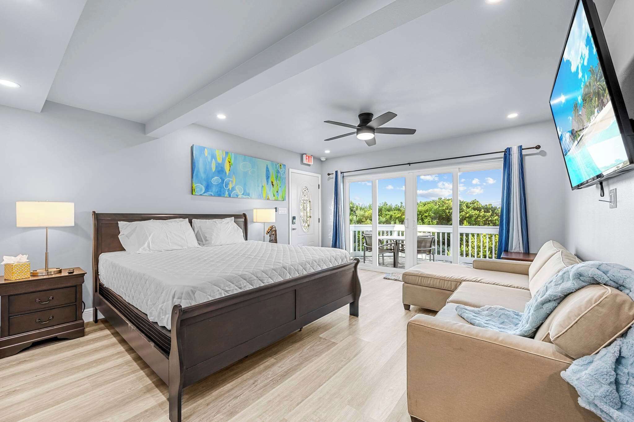 A bedroom with a bed, a nightstand, a TV, a ceiling fan, and a balcony with a view.