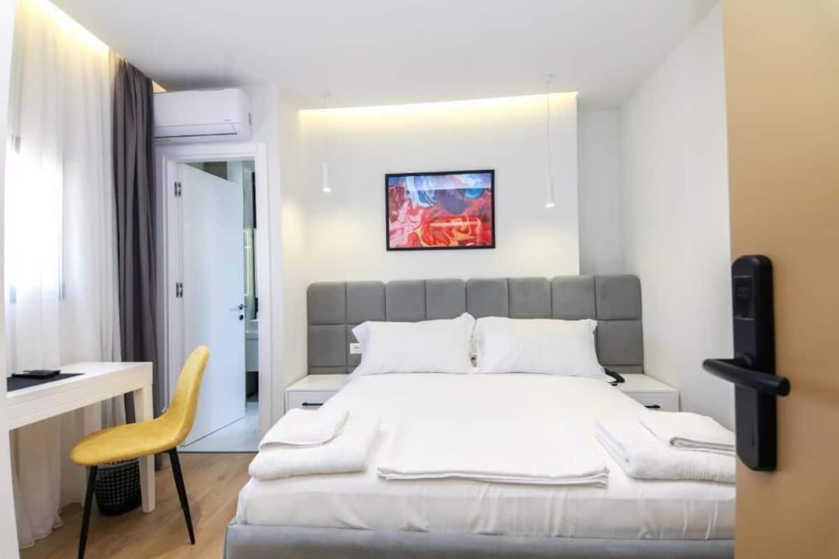A modern hotel room with a bed, bedside tables, a desk, and a chair.