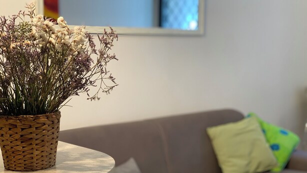 A round table with a woven basket containing dried flowers, a brown sofa with green and yellow cushions, and a framed picture on the wall. - 10 Minutes Walk From San Pietro Excellent for 4 People, Families and Friends (Roma)