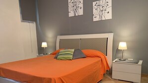 A neatly made bed with an orange bedspread, a gray pillow, and a striped pillow. There are two bedside tables with lamps, a gray rug, and artwork on the wall. - 10 Minutes Walk From San Pietro Excellent for 4 People, Families and Friends (Roma)