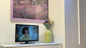 A television on a white cabinet with a framed painting above it and a vase with flowers to the right. - 10 Minutes Walk From San Pietro Excellent for 4 People, Families and Friends (Roma)
