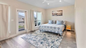 A bedroom with a bed, a ceiling fan, a window with curtains, a nightstand, and a small heater.
