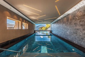 Piscina interior moderna com água cristalina, vista para montanhas e luminárias contemporâneas.