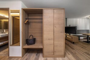 Quarto moderno com guarda-roupa de madeira, um banco, televisão e espelho.