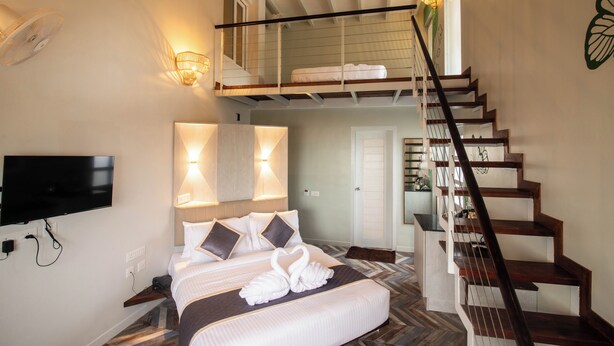 A bedroom with a bed, a TV, a staircase, and a balcony. - La Papillon Maison (Puducherry)
