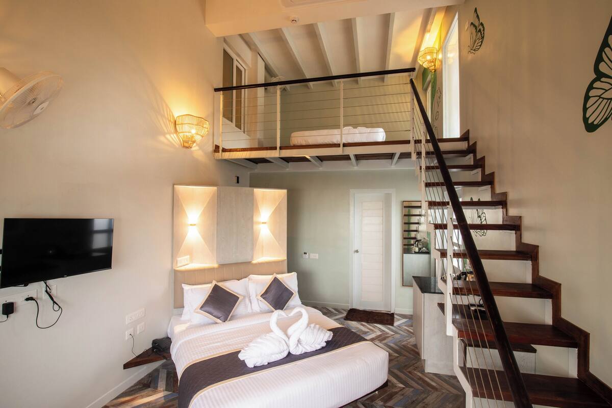 A bedroom with a bed, a TV, a staircase, and a balcony.