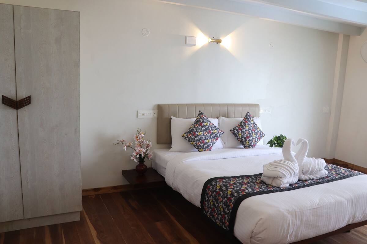 A hotel room with a bed, a nightstand, a vase with flowers, and a wall-mounted light fixture.