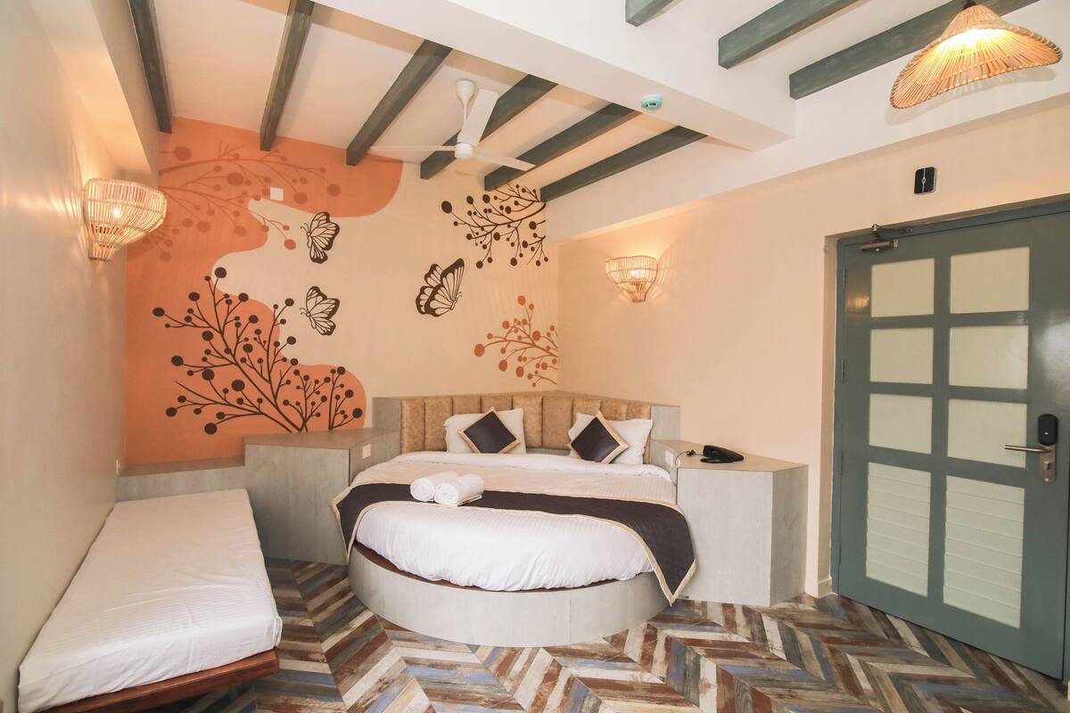 A bedroom with a bed, a bedside table, a chair, a door, and a wall with decorative elements.