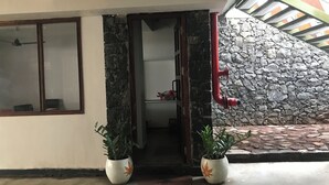 A building entrance with a stone wall, a red pipe, and two potted plants. - La Papillon Maison (Puducherry)