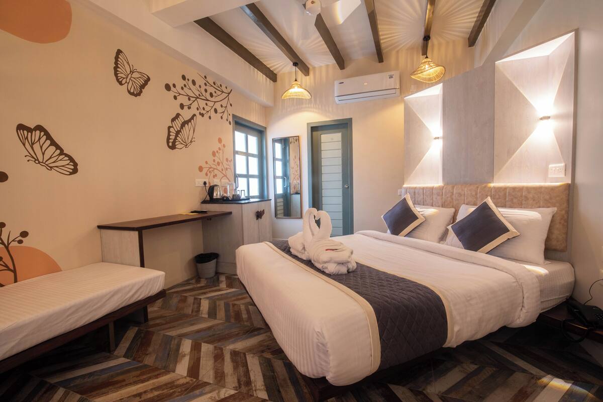 A hotel room with a bed, a desk, and a chair. There are butterfly wall decals, a mirror, and a window.