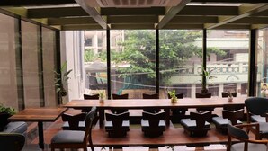 A conference room with a long table and multiple chairs, large windows with a view of greenery and buildings, and potted plants on the table. - La Papillon Maison (Puducherry)