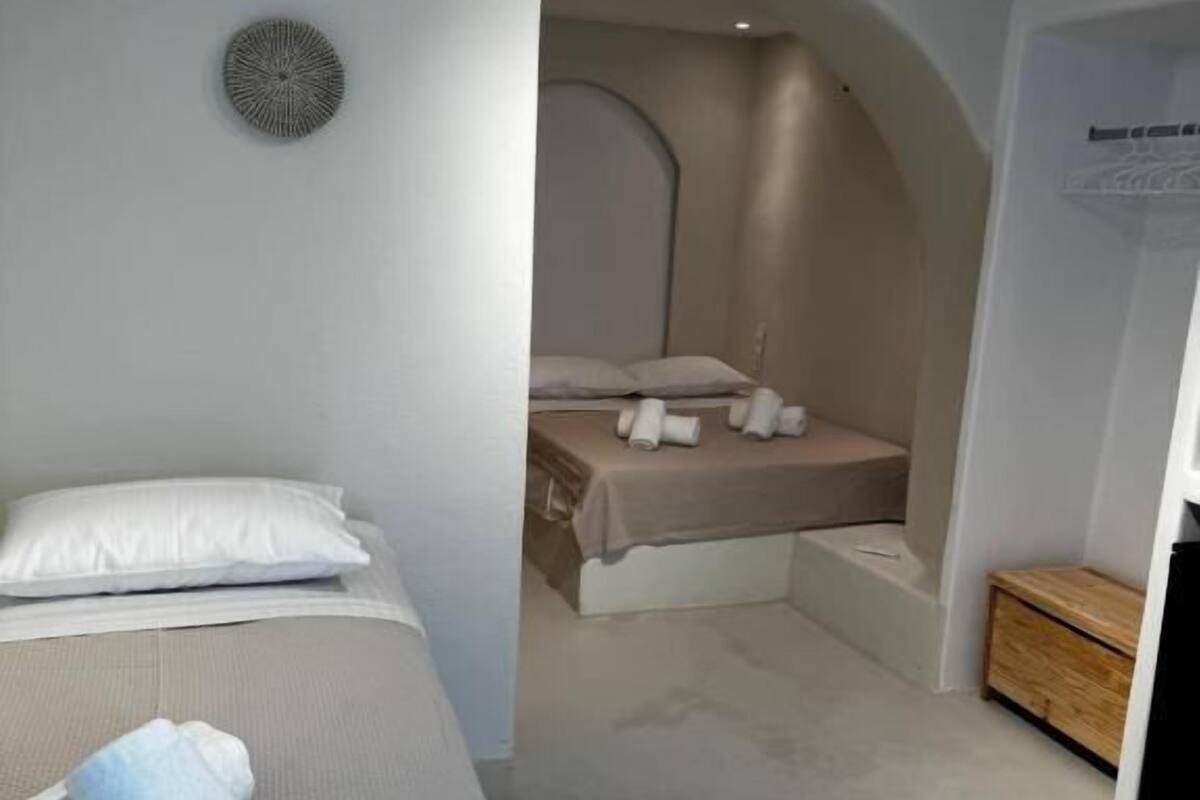 Una camera da letto moderna con un letto grande, un letto più piccolo sullo sfondo e un arredamento minimalista.